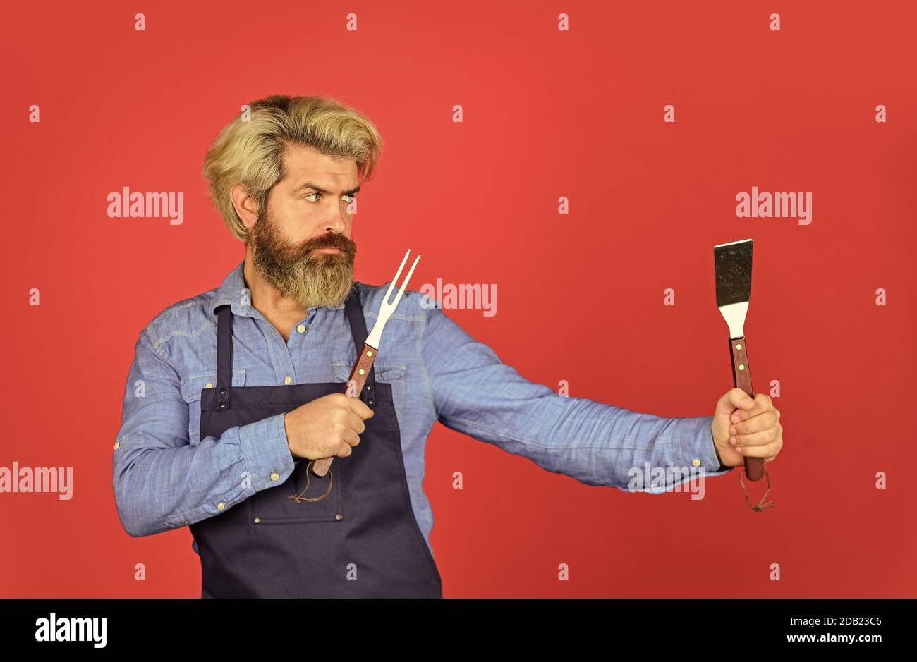 Outils pour rôtir la viande. Qui cuisinent mieux. Le défi ultime de la cuisine. Préparez le dîner pour la famille. Utilisez des ustensiles de cuisine et divers produits. Le chef mûr utilise des ustensiles de cuisine pour le barbecue. Banque D'Images