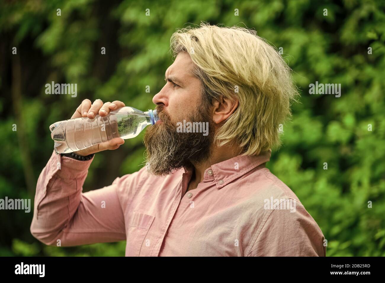 Chaleur estivale. Boire de l'eau claire. Sécurité et santé. Équilibre de l'eau. Homme barbu touriste eau potable bouteille plastique nature fond. Un gars assoiffé qui boit de l'eau en bouteille Un mode de vie sain. Banque D'Images