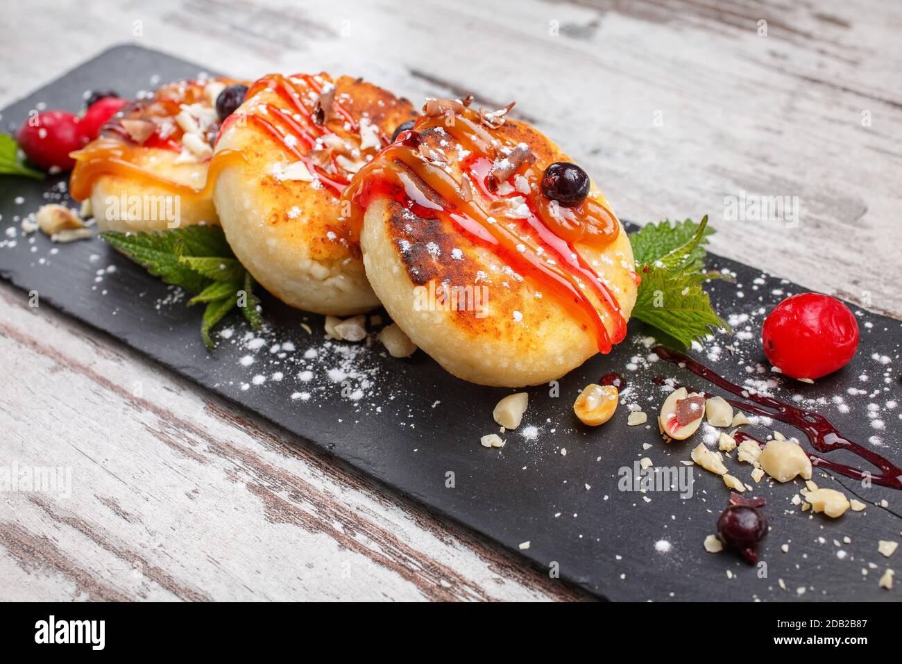 Beignets doux avec confiture sur un tableau en pierre. Fond en bois simple. Crêpes avec confiture et sucre en poudre. Décoré de feuilles de menthe verte et de cerises. Banque D'Images