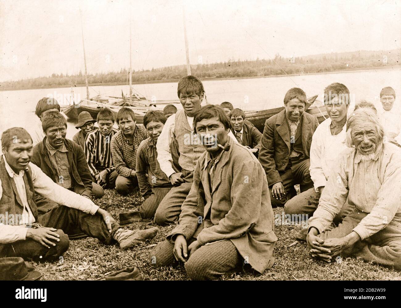 Hommes et garçons indiens vêques de l'Ouest, assis le long du rivage, bateaux en arrière-plan. Banque D'Images