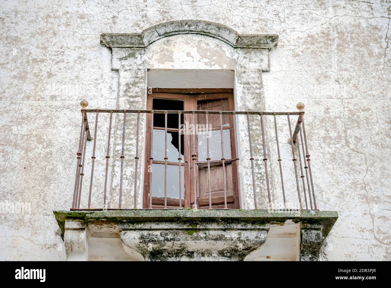 Fenêtre avec accès au vieux balcon et clôture en fer forgé forgé par le passage du temps sur une façade d'une maison ancienne et rustique Banque D'Images