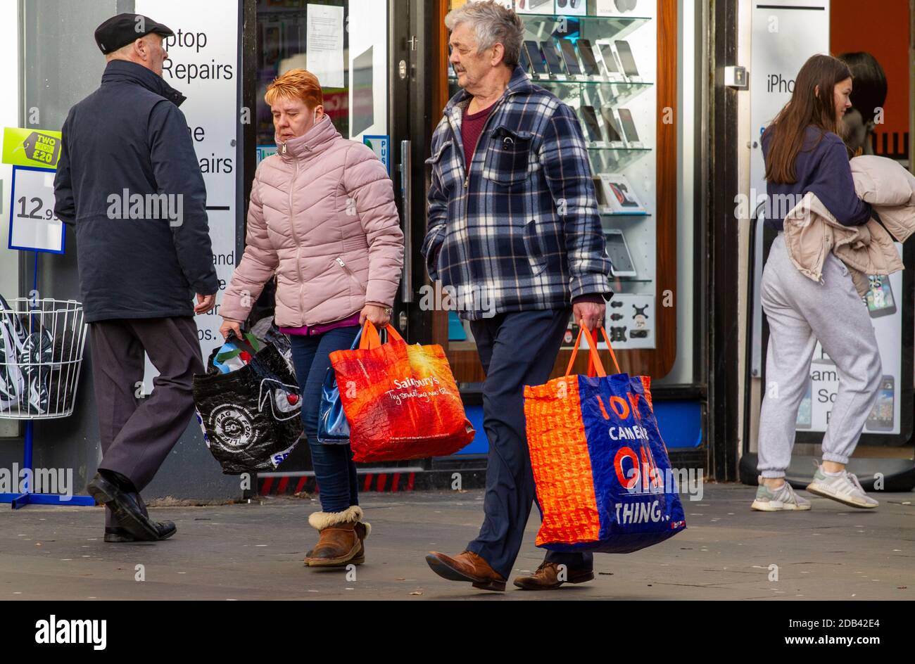 Dundee, Tayside, Écosse, Royaume-Uni. 16 novembre 2020. UK News Covid-19 Lockdown. Les personnes qui marchent dans les rues de Dundee avec peu de magasins de vêtements essentiels ouverts depuis que la restriction plus stricte de niveau 3 Covid-19 Lockdown a été appliquée. Un couple est conscient des directives de distanciation sociale et du port de masques de visage marchant ensemble avec de grands porte-bagages de marque lors de leurs achats de début de Noël dans le centre-ville dans un après-midi froid et ensoleillé de novembre. Crédit : Dundee Photographics/Alamy Live News Banque D'Images