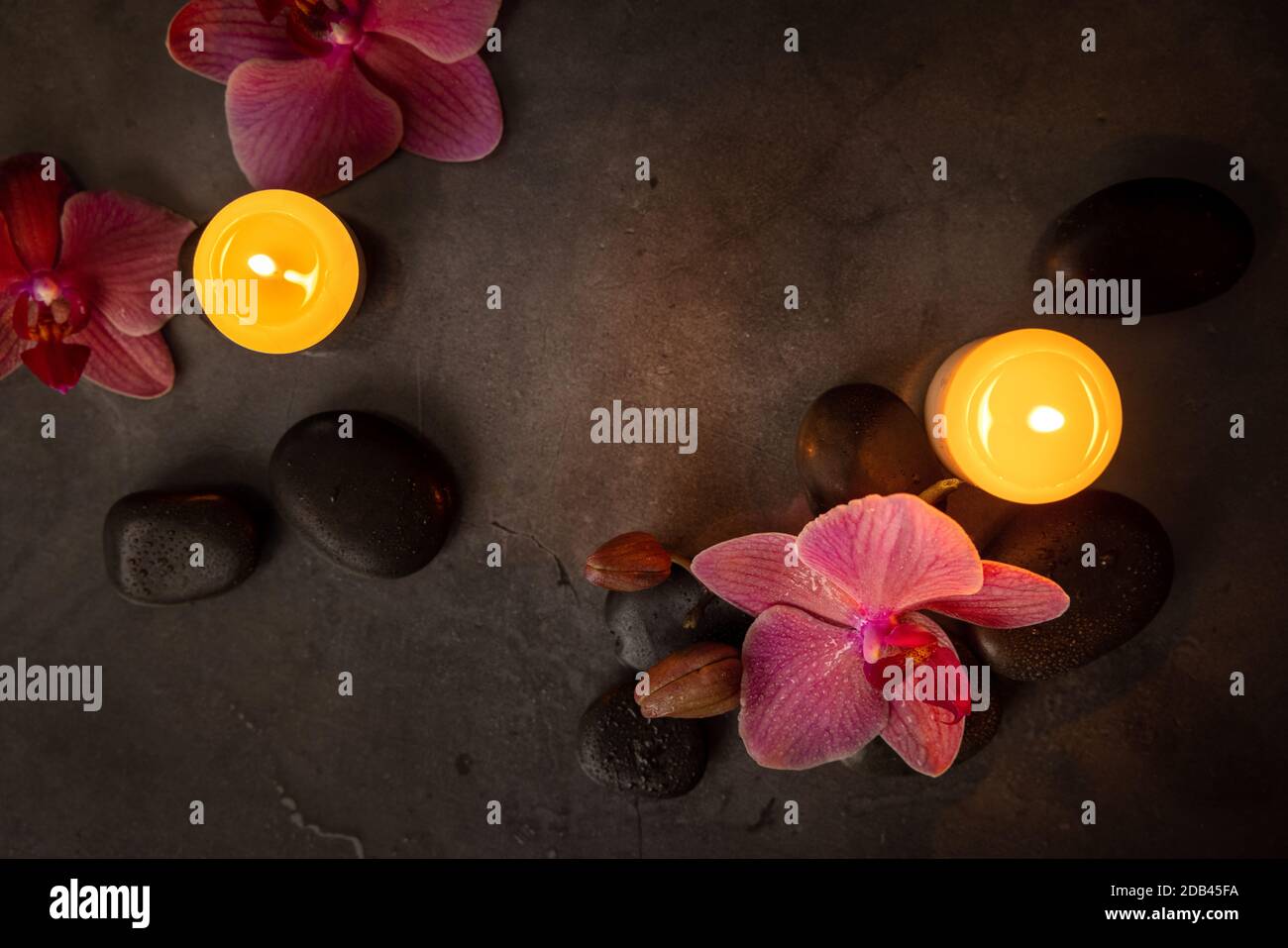 fleurs d'orchidées avec pierres de spa et bougies sur fond de roche sombre. soin de beauté et concept de bien-être. vue sur le dessus Banque D'Images