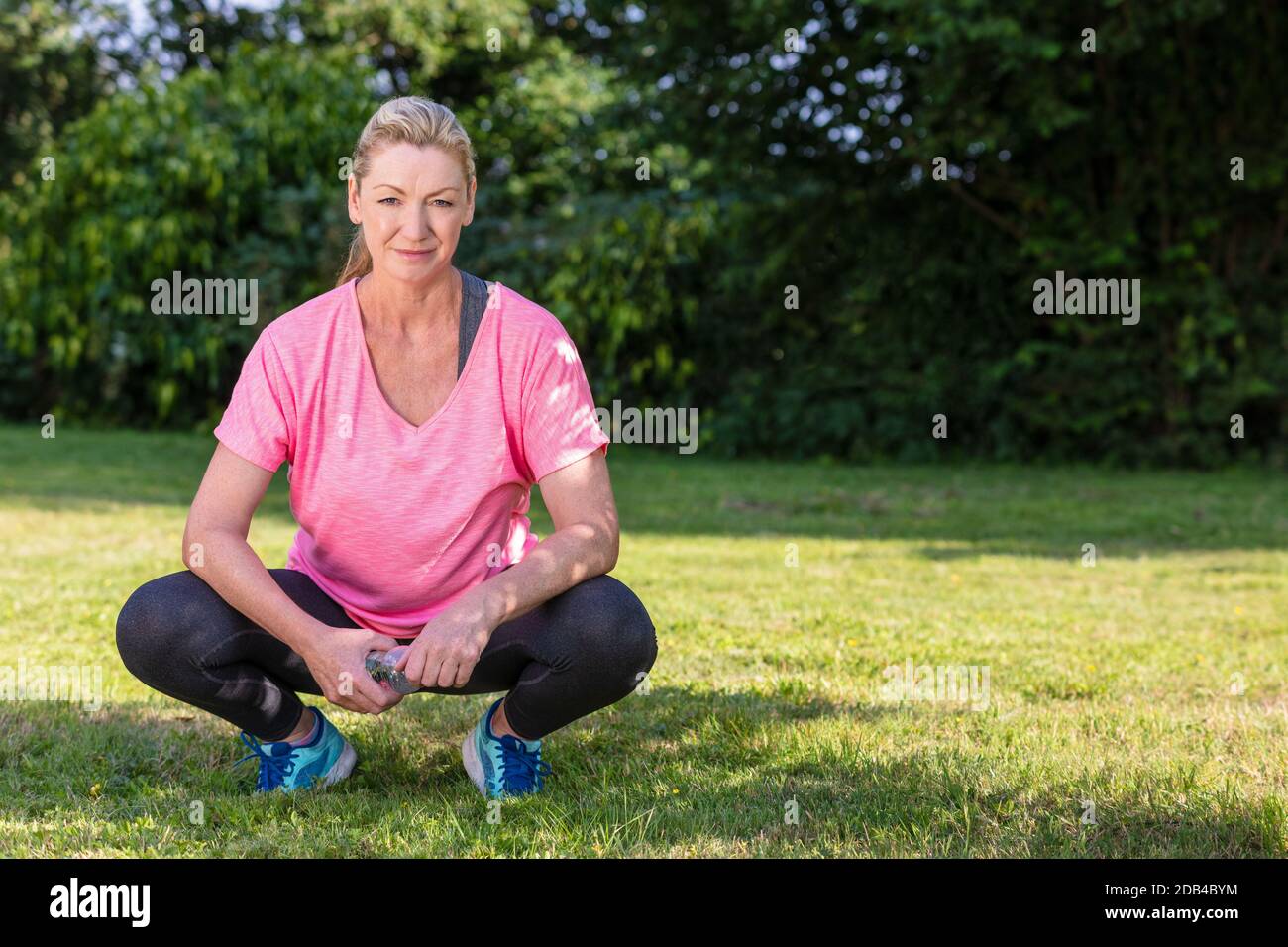 Portrait extérieur d'une jolie femme blonde d'âge moyen souriant buvant de l'eau se détendant après l'exercice, la course à pied ou le style de vie de forme physique Banque D'Images