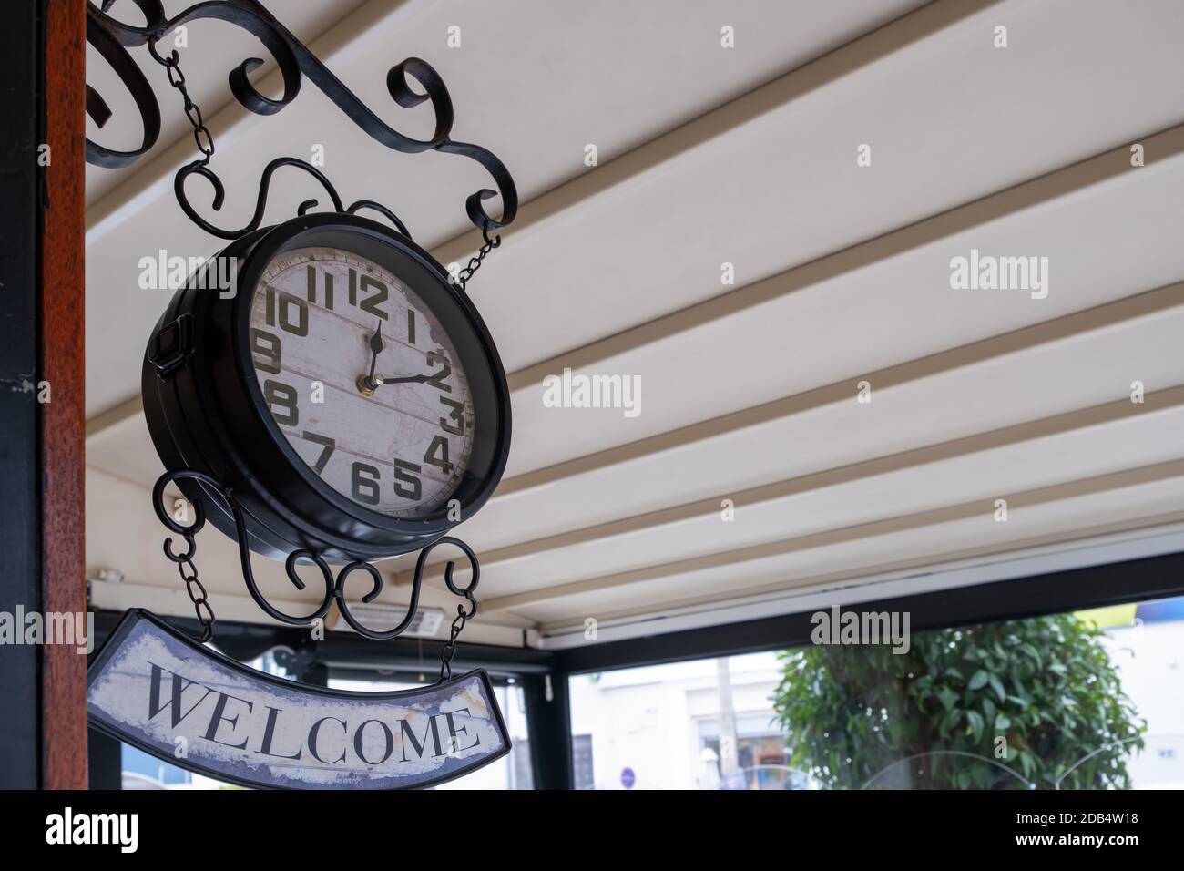 Affiche de bienvenue, horloge vintage. Vue à angle bas de l'horloge rétro miteuse suspendue sous le toit sur le porche à l'extérieur de la boutique Banque D'Images