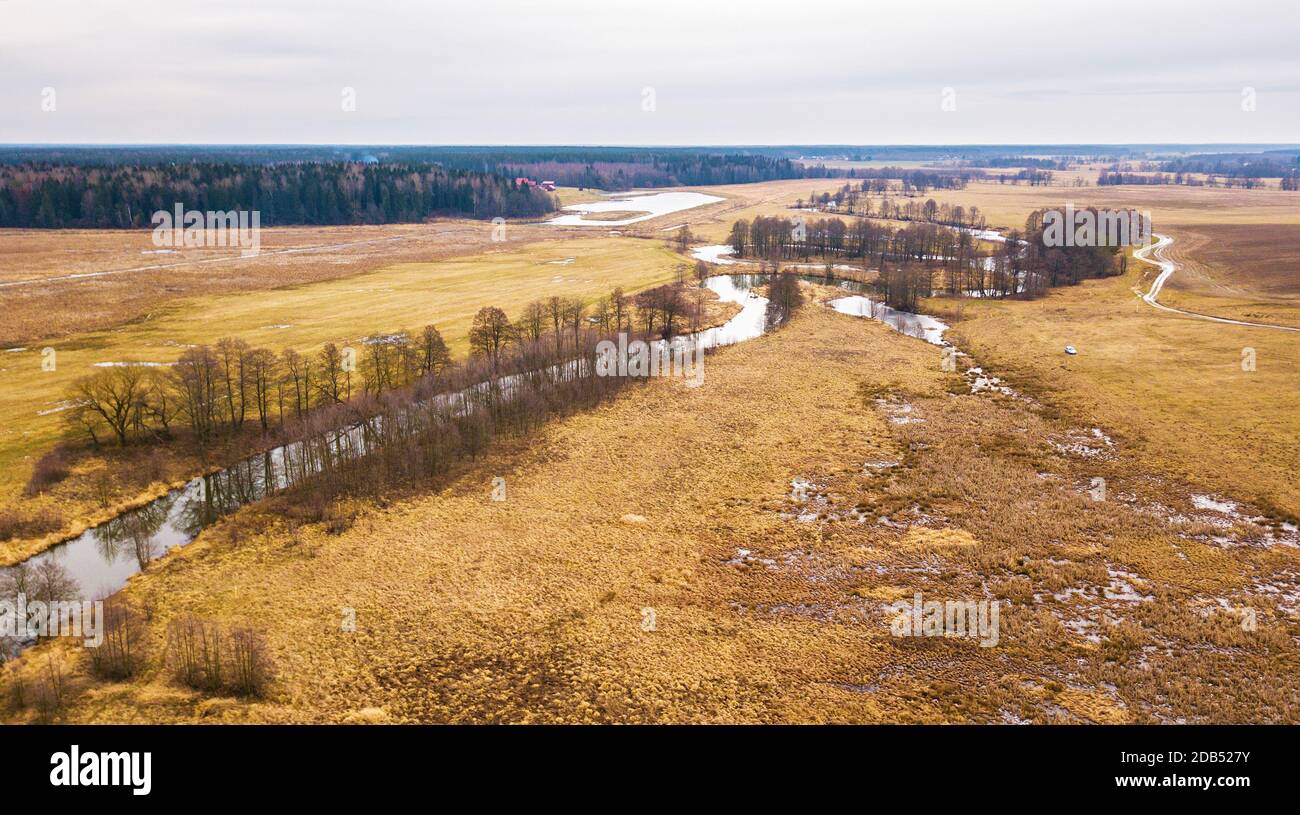 Petite rivière avec arbres secs sans feuilles en hiver / vue aérienne du début du printemps. Temps déprimé. Terres agricoles, jardins et champs de la région de Minsk, Banque D'Images