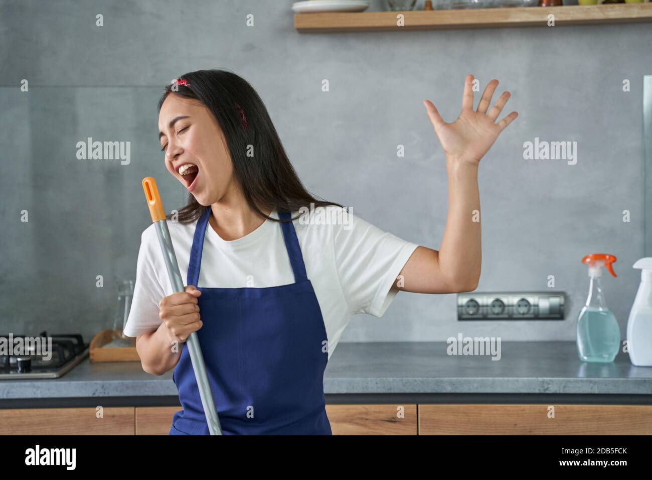 Amuse-toi bien. Portrait de la jeune femme joyeuse, femme de nettoyage prétendant chanter, tenant le balai tout en nettoyant le sol, faisant des tâches ménagères. Le concept de ménage et de ménage Banque D'Images