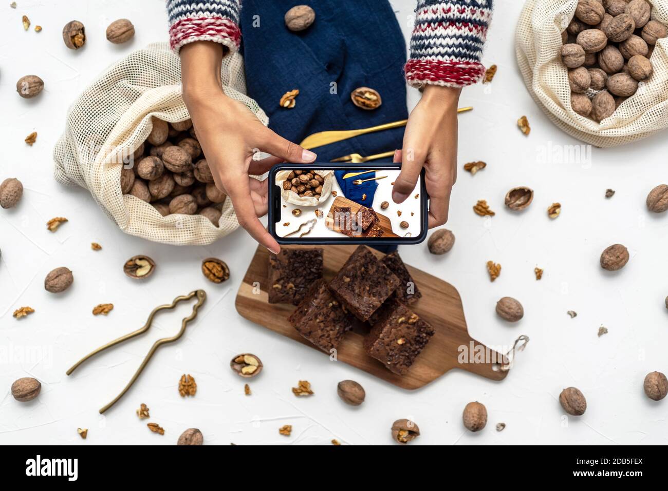 Les mains de la femme prennent des photos avec un smartphone de brownies maison sur fond blanc avec écrous Banque D'Images