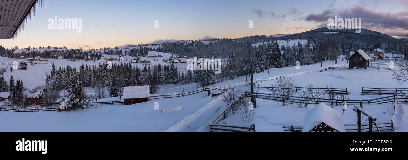 Avant l'aube, petit village alpin tranquille et hiver, montagnes enneigées autour de la vue panoramique. Partie du toit avec des glaçons comme symbole du confort de la maison. Banque D'Images