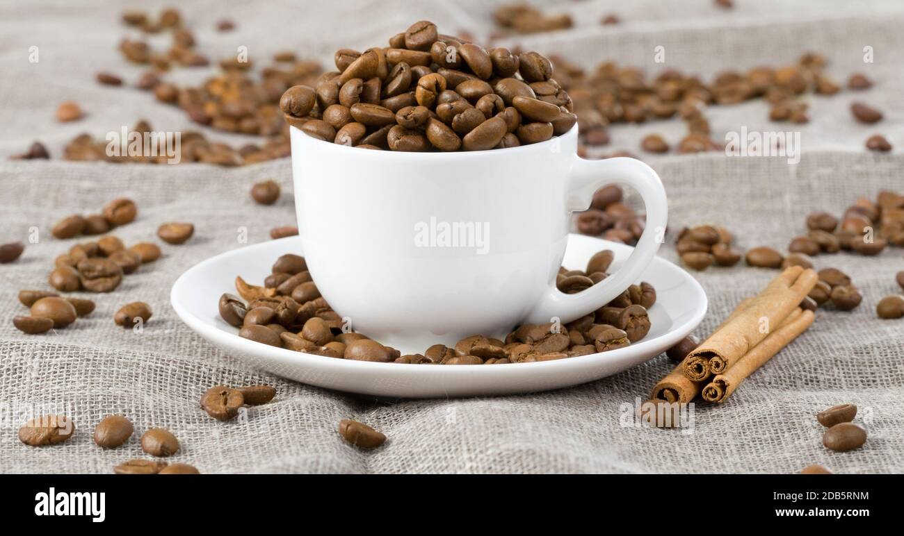 versé dans une tasse blanche torréfiée grains de café très savoureux sur une nappe, à côté de lui sont des bâtons de cannelle odorante et agréable Banque D'Images