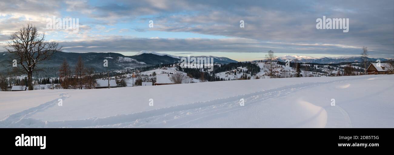 Petit village alpin et hiver montagne enneigée au premier lever du soleil autour, Voronenko, Carpates, Ukraine. Tracer sur un chemin fraîchement trodden à travers g Banque D'Images