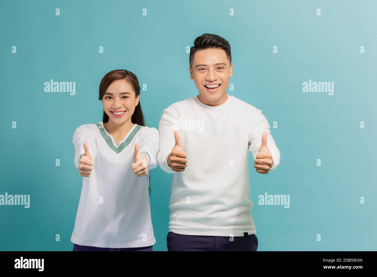 Un jeune couple heureux qui montre ses pouces et regarde l'appareil photo isolé sur fond bleu Banque D'Images
