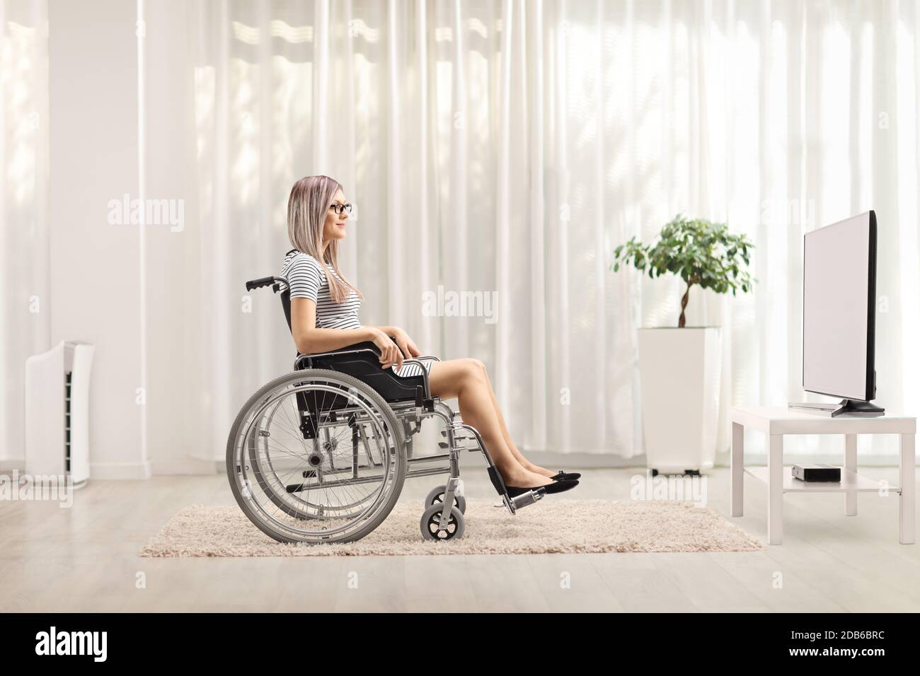 Photo d'une jeune femme blonde en fauteuil roulant regarder la télévision Banque D'Images
