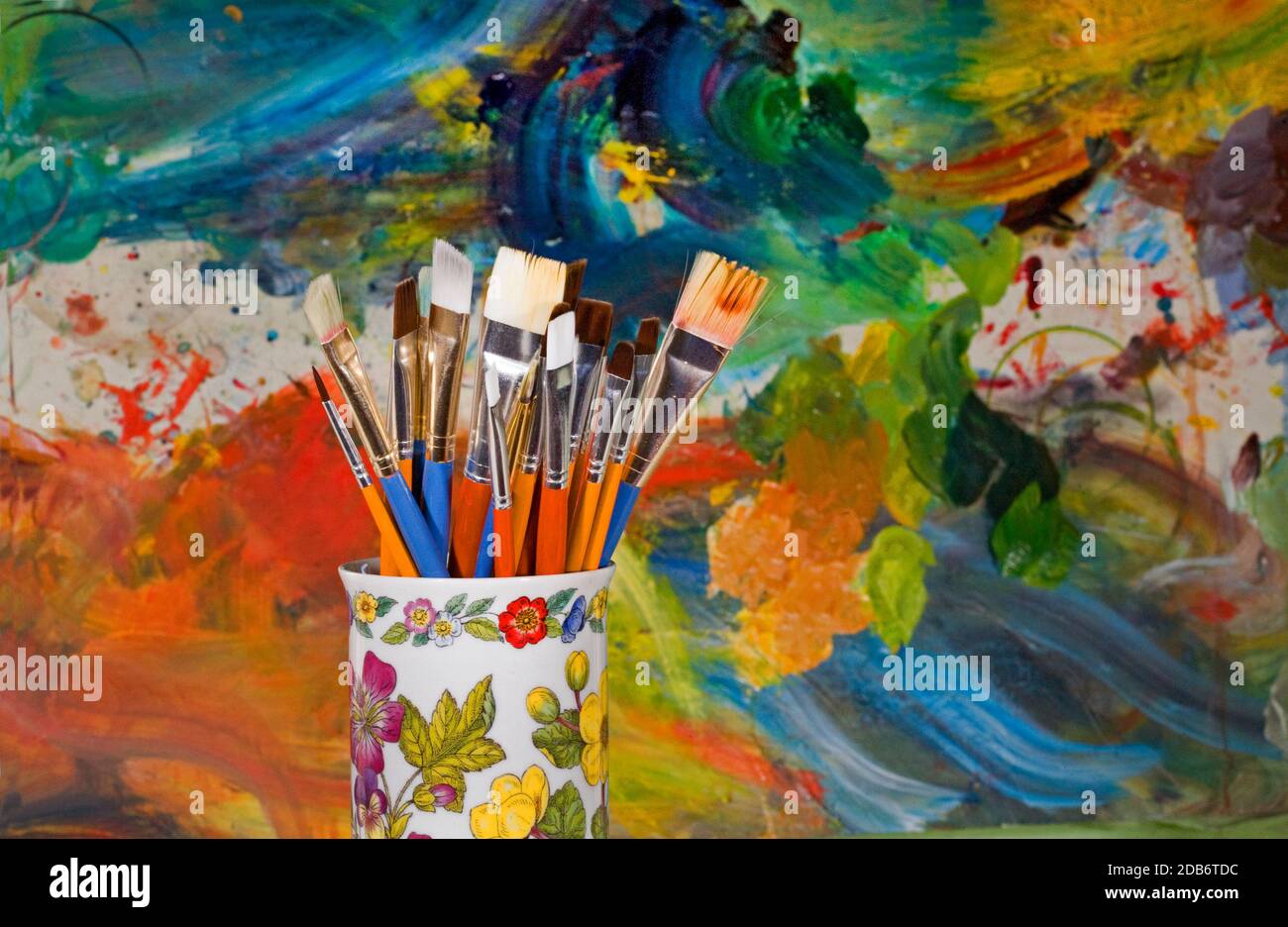 Un groupe de pinceaux artistiques de différentes tailles dans un support de couleur vive devant la palette du peintre. Banque D'Images
