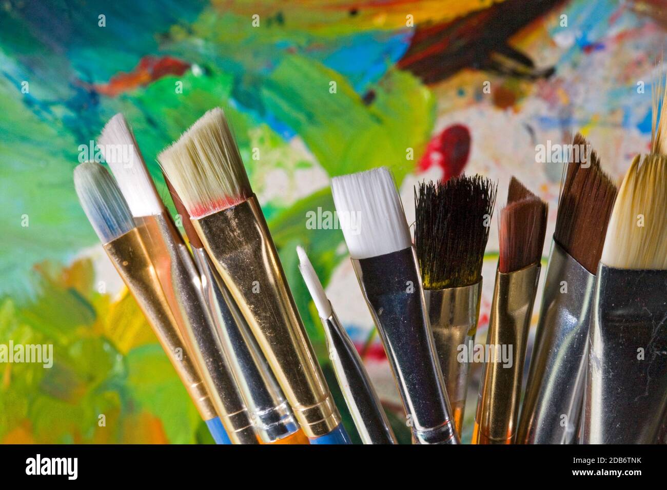 Un groupe de pinceaux artistiques de différentes tailles dans un support de couleur vive devant la palette du peintre. Banque D'Images