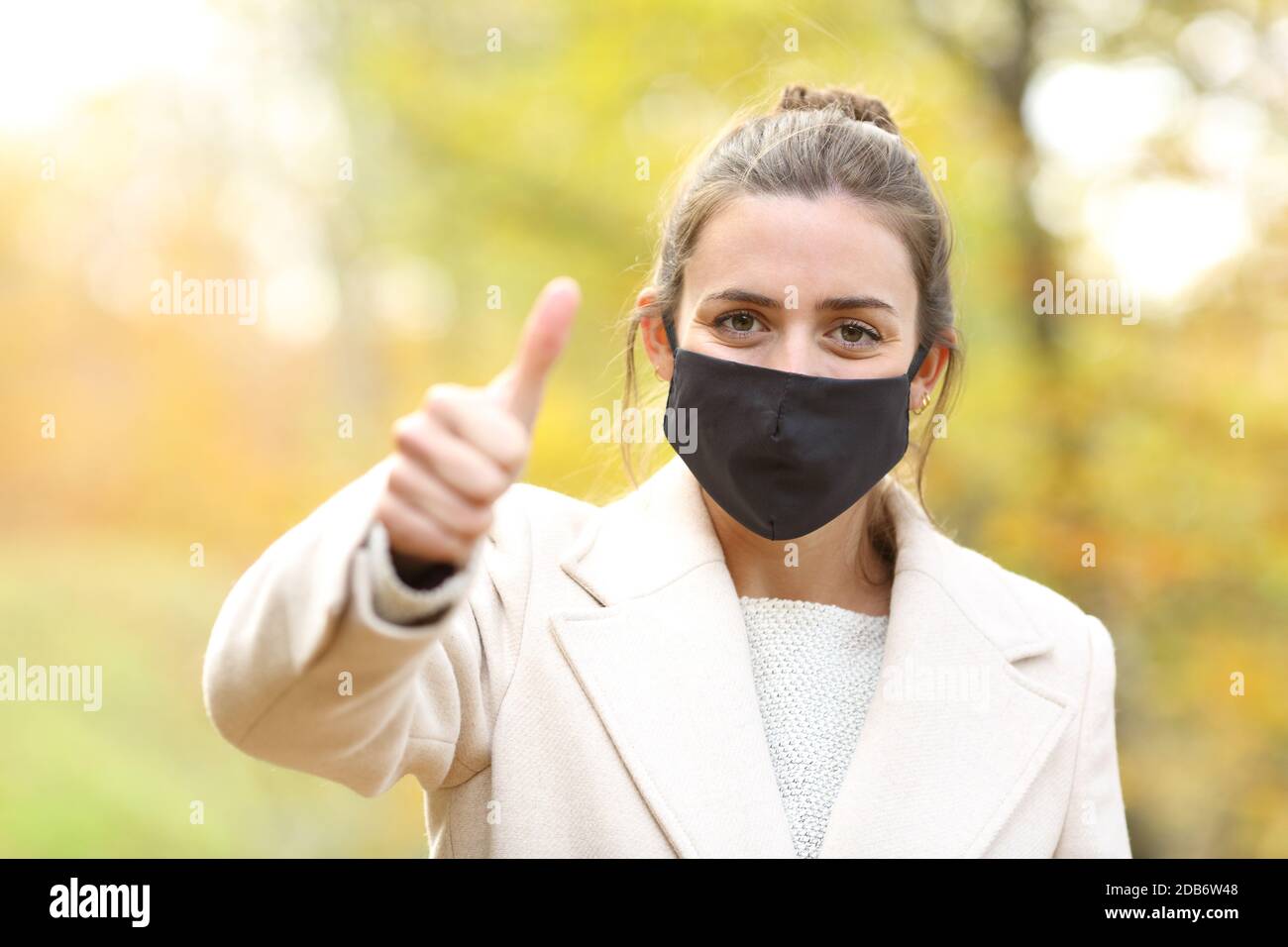 Bonne femme avec masque gestante pouce debout dans un parc en automne Banque D'Images