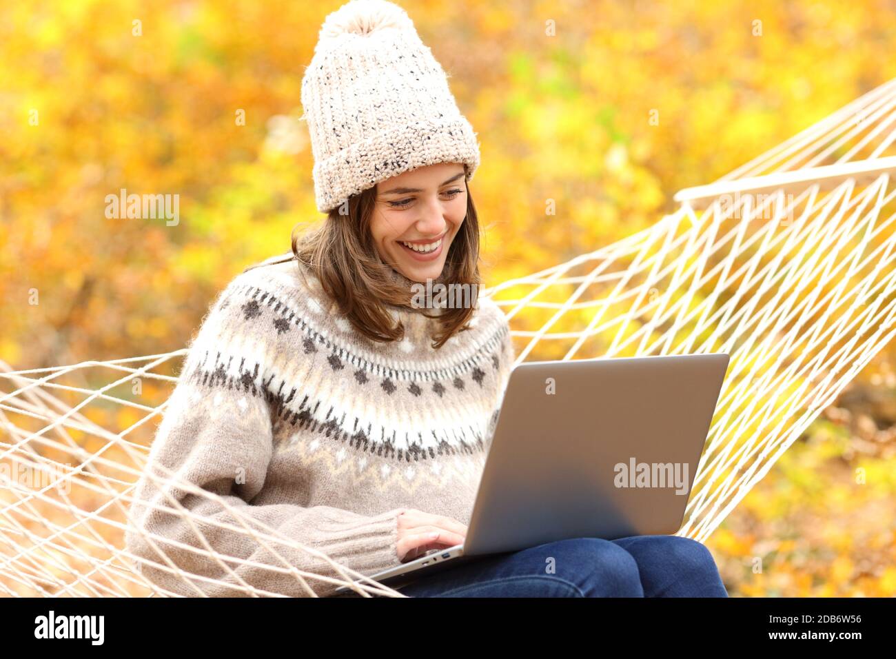 Bonne femme utilisant un ordinateur portable assis sur un hamac en automne dans une forêt Banque D'Images