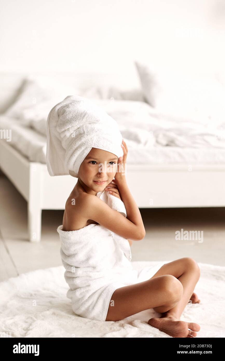 Routine du matin. Une petite fille enveloppée d'une serviette blanche après  qu'une douche s'assoit sur la moquette au sol chaud dans une chambre  lumineuse. Beauté, spa et hygiène Photo Stock - Alamy