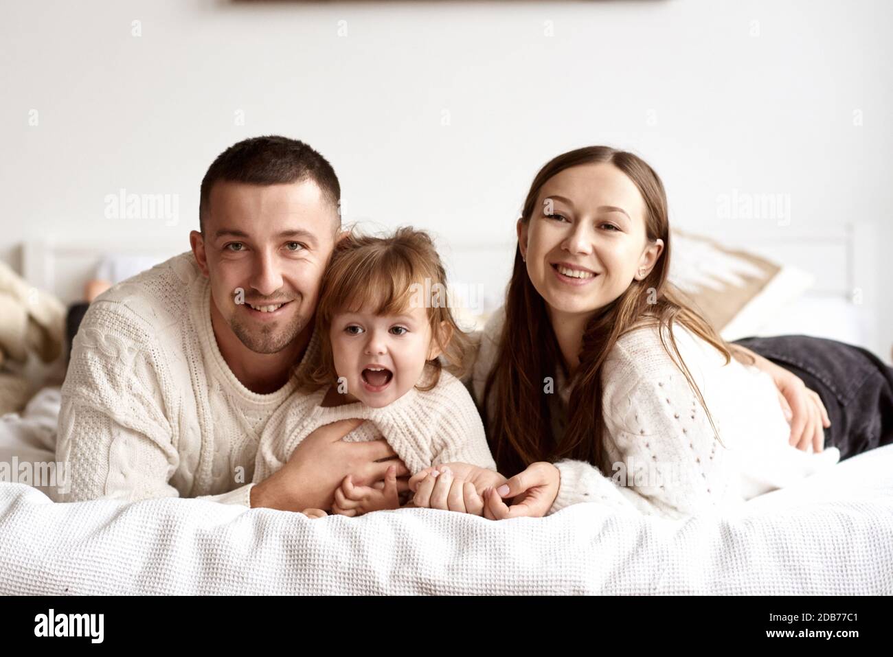 Portrait d'une jeune famille heureuse couché au lit souriant et regardant l'appareil photo. Banque D'Images