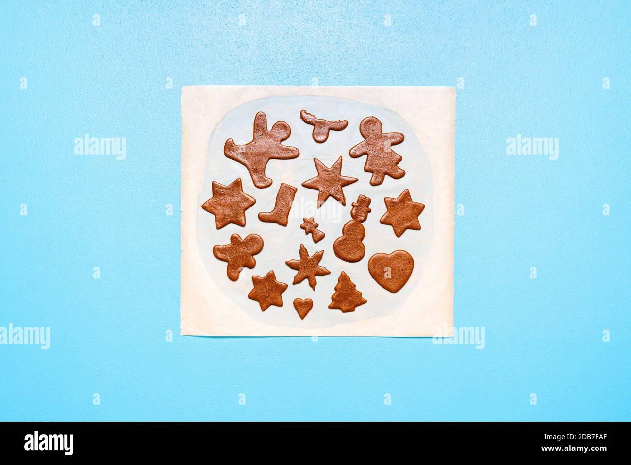 Biscuits à cuire plat déposer avec de la pâte de pain d'épice coupée dans de nombreuses formes, sur un papier de cuisson, sur fond bleu. Biscuits en forme d'étoile et de pain d'épice crus. Banque D'Images