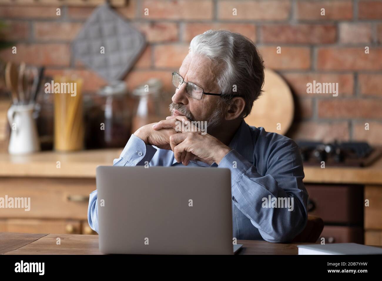 Homme mûr et réfléchi portant des lunettes sur un ordinateur portable, regardant de côté Banque D'Images