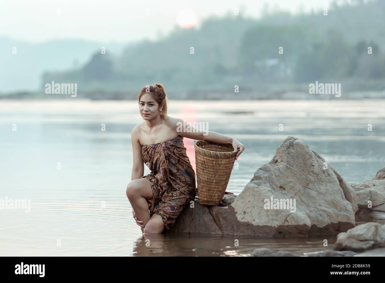 Femme assise sur un rocher au bord d'une rivière, Thaïlande Banque D'Images