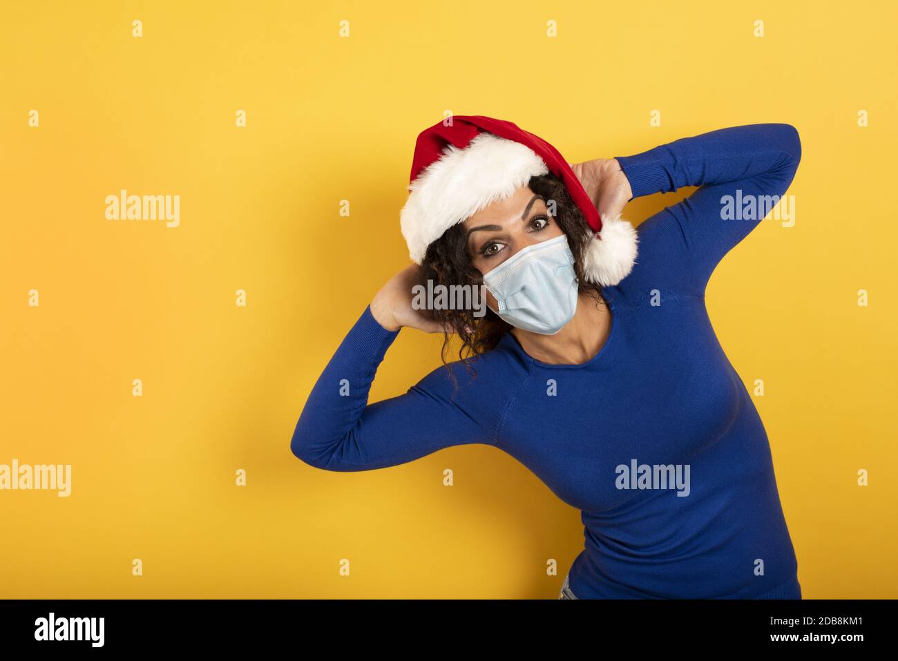 Bonne femme avec un chapeau de Noël et un masque pour être protégée contre le covid-19. Arrière-plan de yelow Banque D'Images