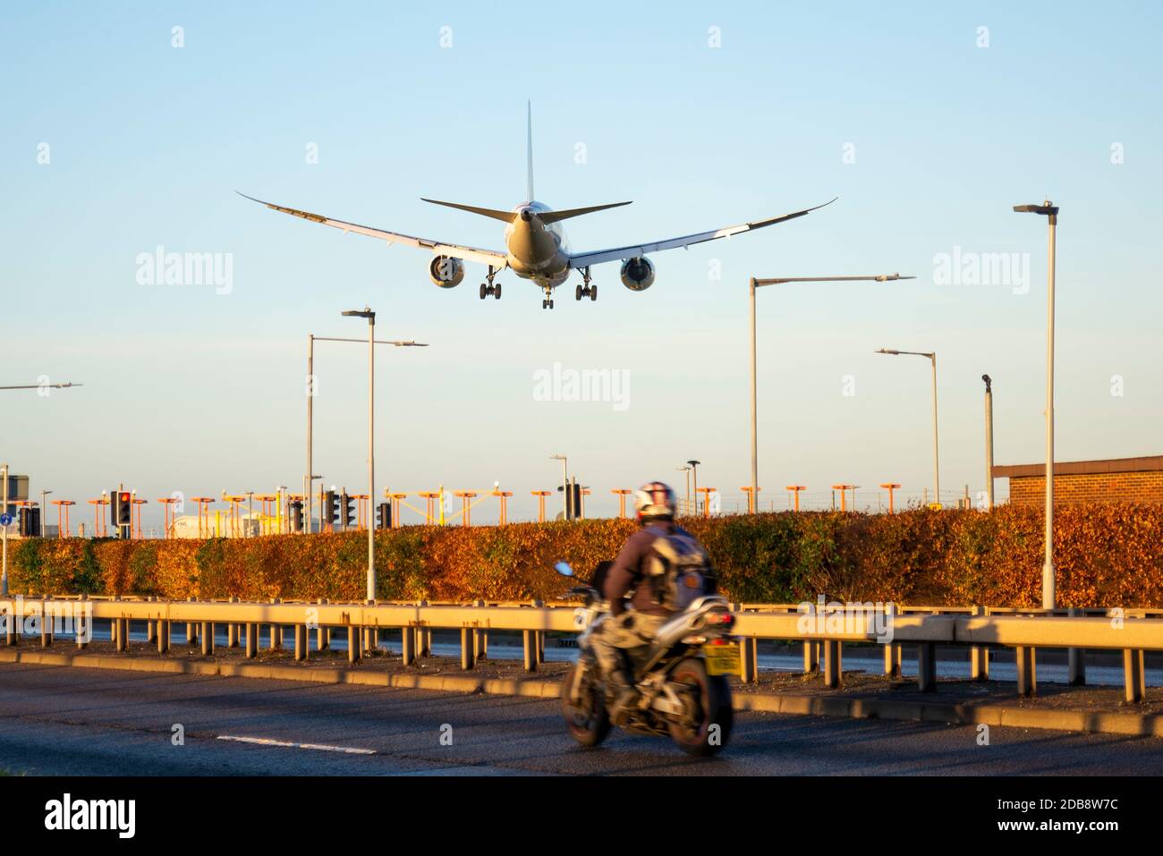 Atterrissage en avion de ligne à l'aéroport de Londres Heathrow, Royaume-Uni, à l'aube, le matin ensoleillé de l'automne. Arrivée anticipée. Sur la route A30 avec un motocycliste passant Banque D'Images
