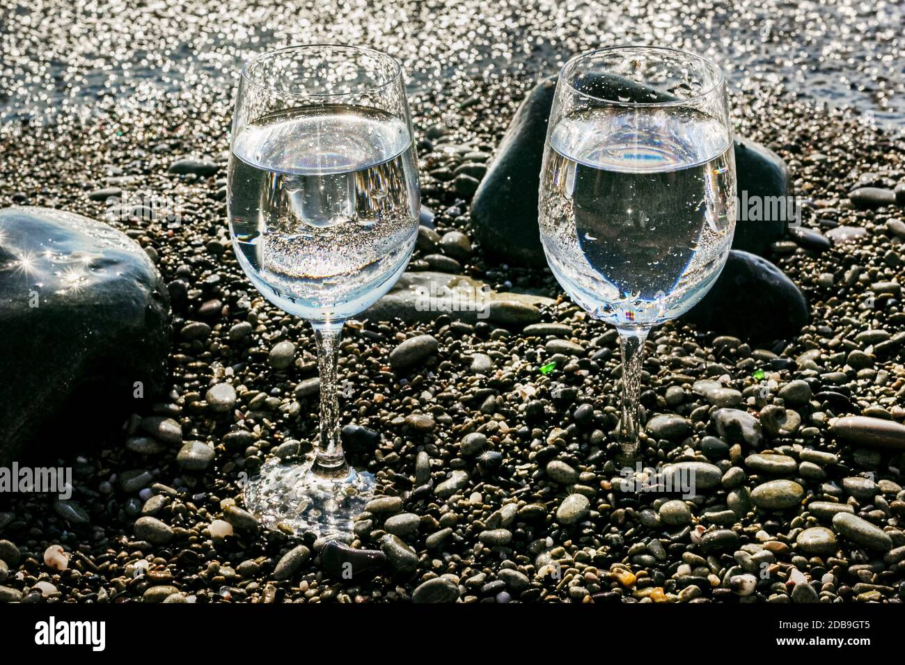 Deux jolis verres d'eau sur des cailloux de mer par l'eau Banque D'Images