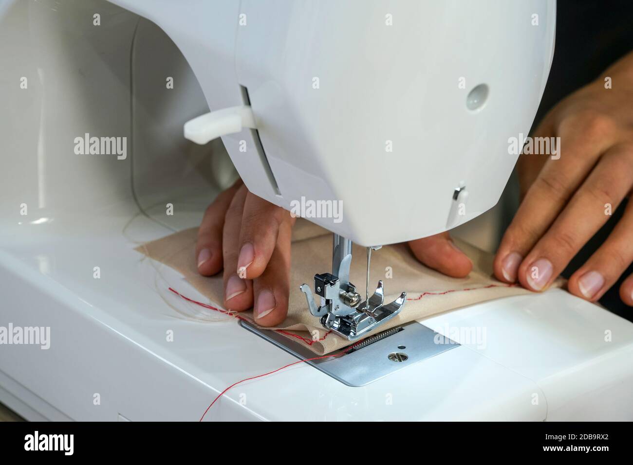 La couturière de créateur de mode est décorée avec soin d'un motif rouge en soie sur un tissu beige fin. Banque D'Images