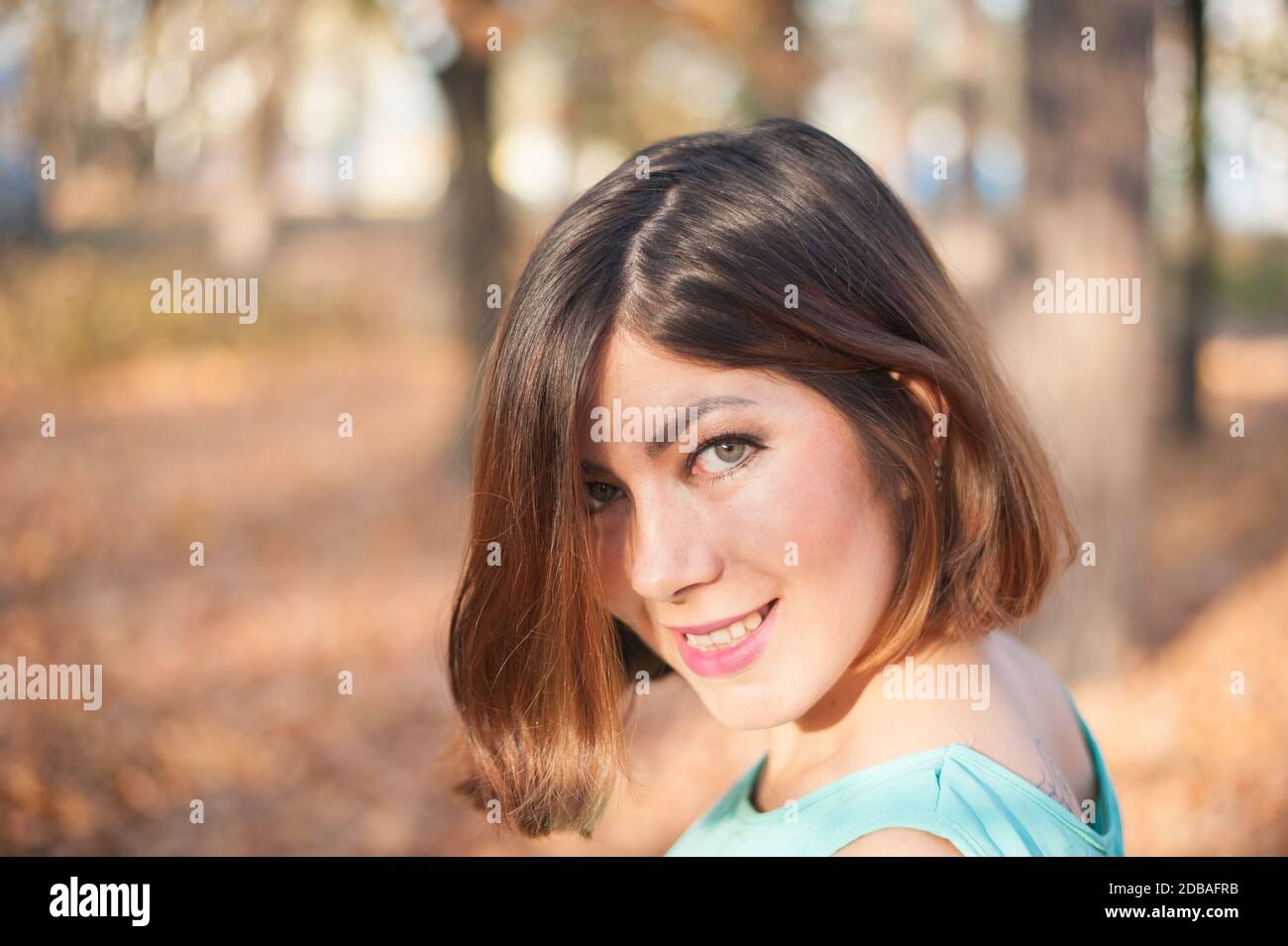 jolie fille aux cheveux sombres et aux sourires bleus, regarde son épaule dans le parc en automne Banque D'Images