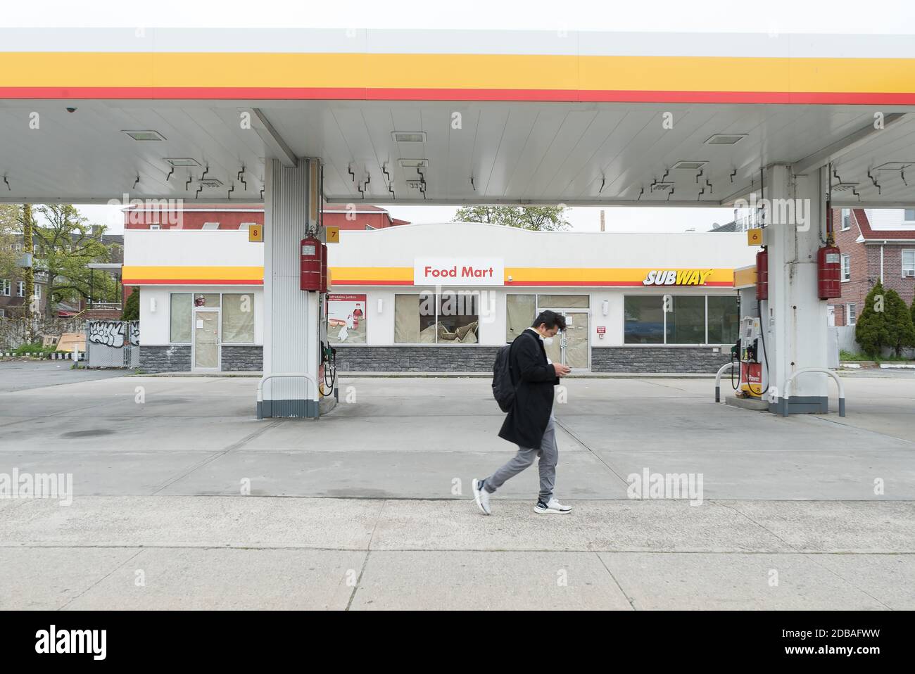Un homme portant un masque marche à côté d'une station-service vide hors-d'affaires sur Northern Boulevard à Sunnyside, Queens. Banque D'Images Un homme portant un masque marche à côté d'une station-service vide hors-d'affaires sur Northern Boulevard à Sunnyside, Queens. Banque D'Images