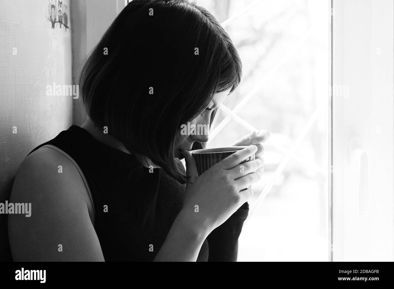 portrait noir et blanc d'une jeune fille de brunette en noir avec une grande tasse de thé par la fenêtre Banque D'Images