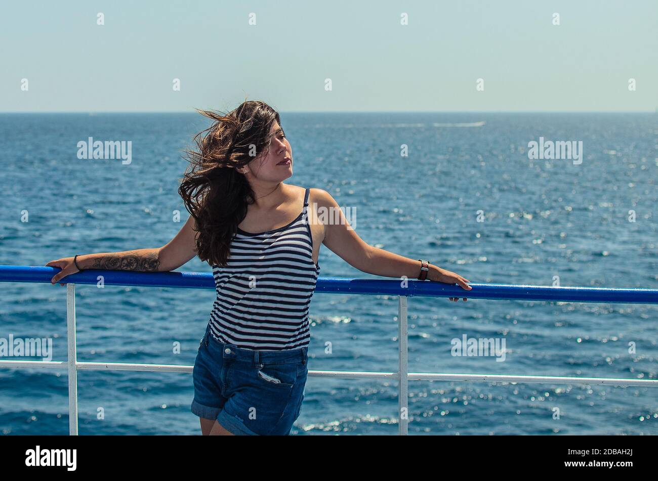 jolie jeune femme brunette dans un débardeur rayé et un short en denim bleu apprécie la mer sur le pont d'un bateau Banque D'Images