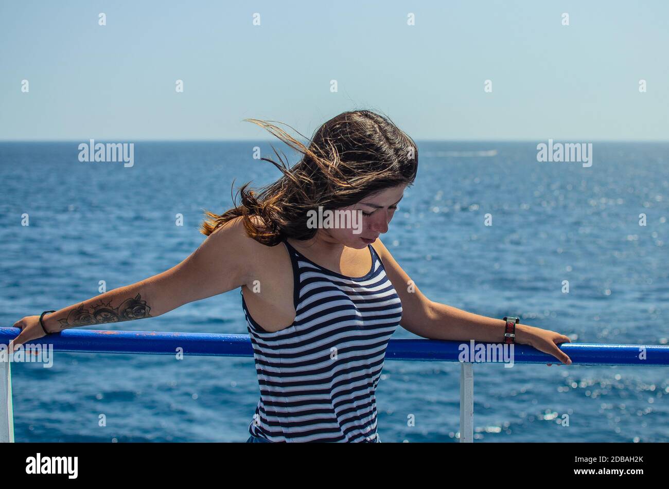 Portrait d'une jolie jeune fille avec des cheveux noirs avec un tatouage sur son bras dans un T-shirt rayé serré sur un fond de mer bleue Banque D'Images