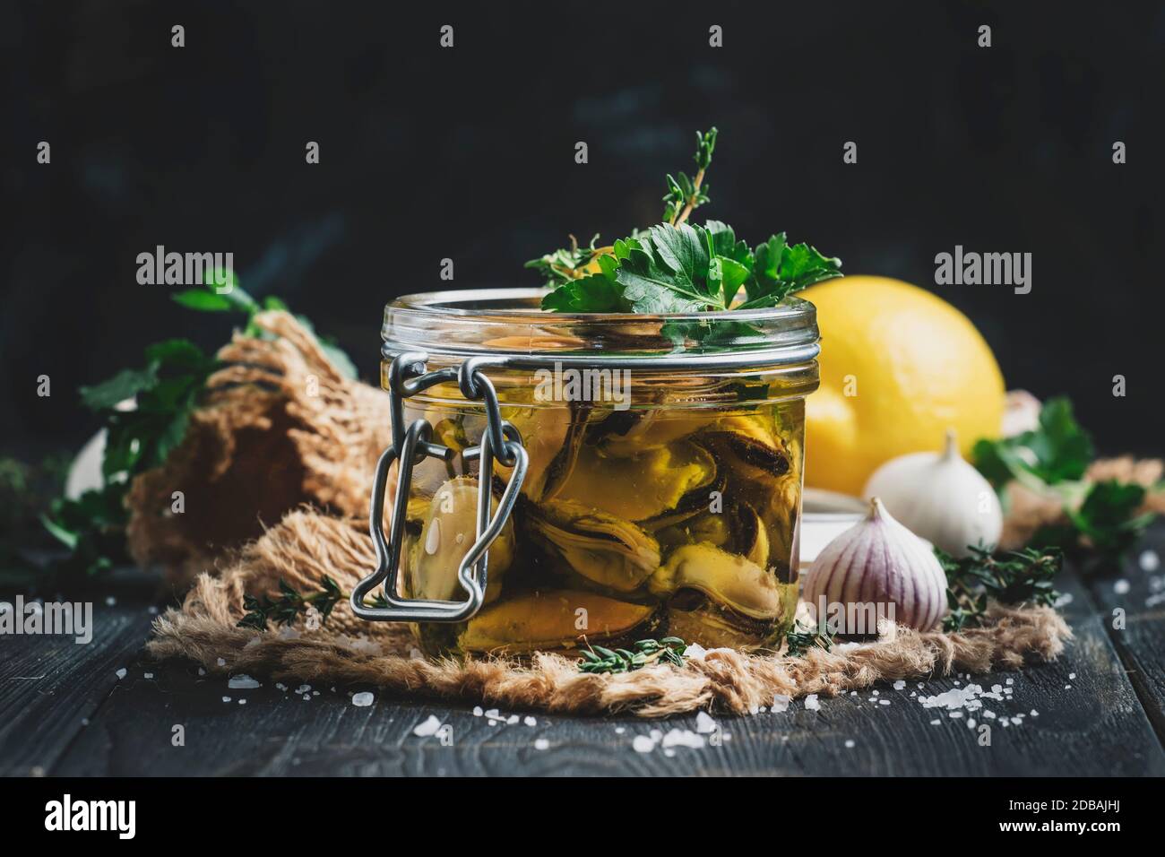 Moules en conserve dans l'huile d'olive et jus de citron avec épices, ail et herbes, table de cuisine en bois noir, foyer sélectif Banque D'Images