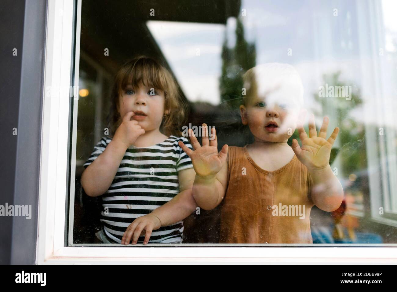 Portrait de la petite fille (2-3) et du bébé garçon (18-23 mois) debout derrière la fenêtre Banque D'Images