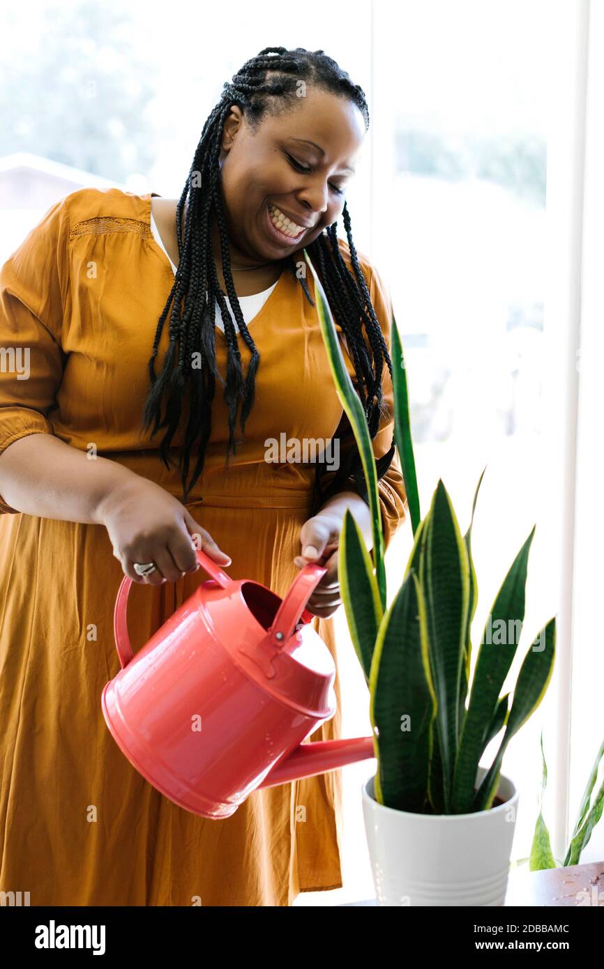 Femme souriante en robe orange arrosoir plante en pot à la maison Banque D'Images