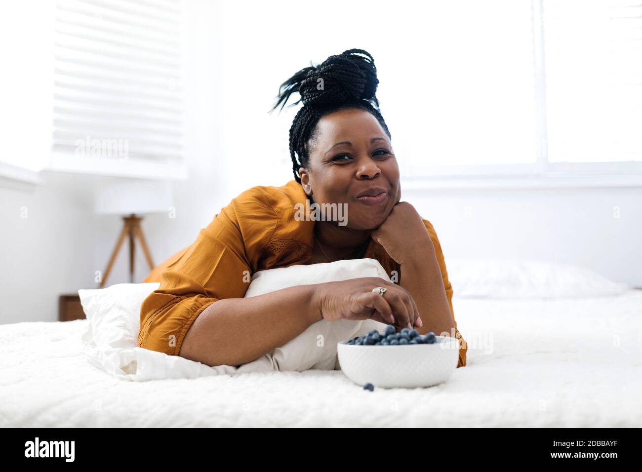 Femme couché sur le lit, mangeant des myrtilles et regardant la télévision Banque D'Images