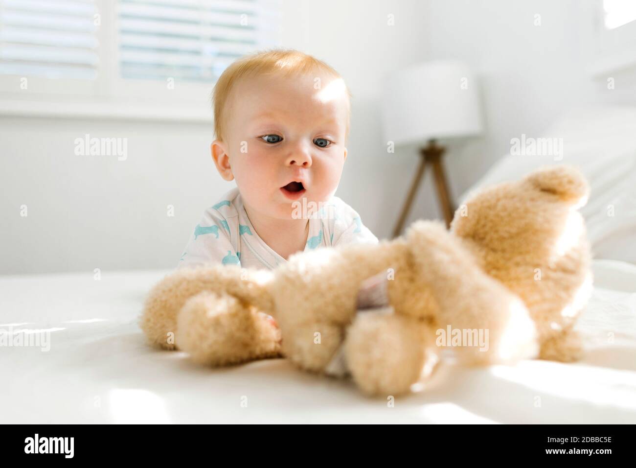 Bébé garçon (6-11 mois) regardant l'ours en peluche sur le lit Banque D'Images