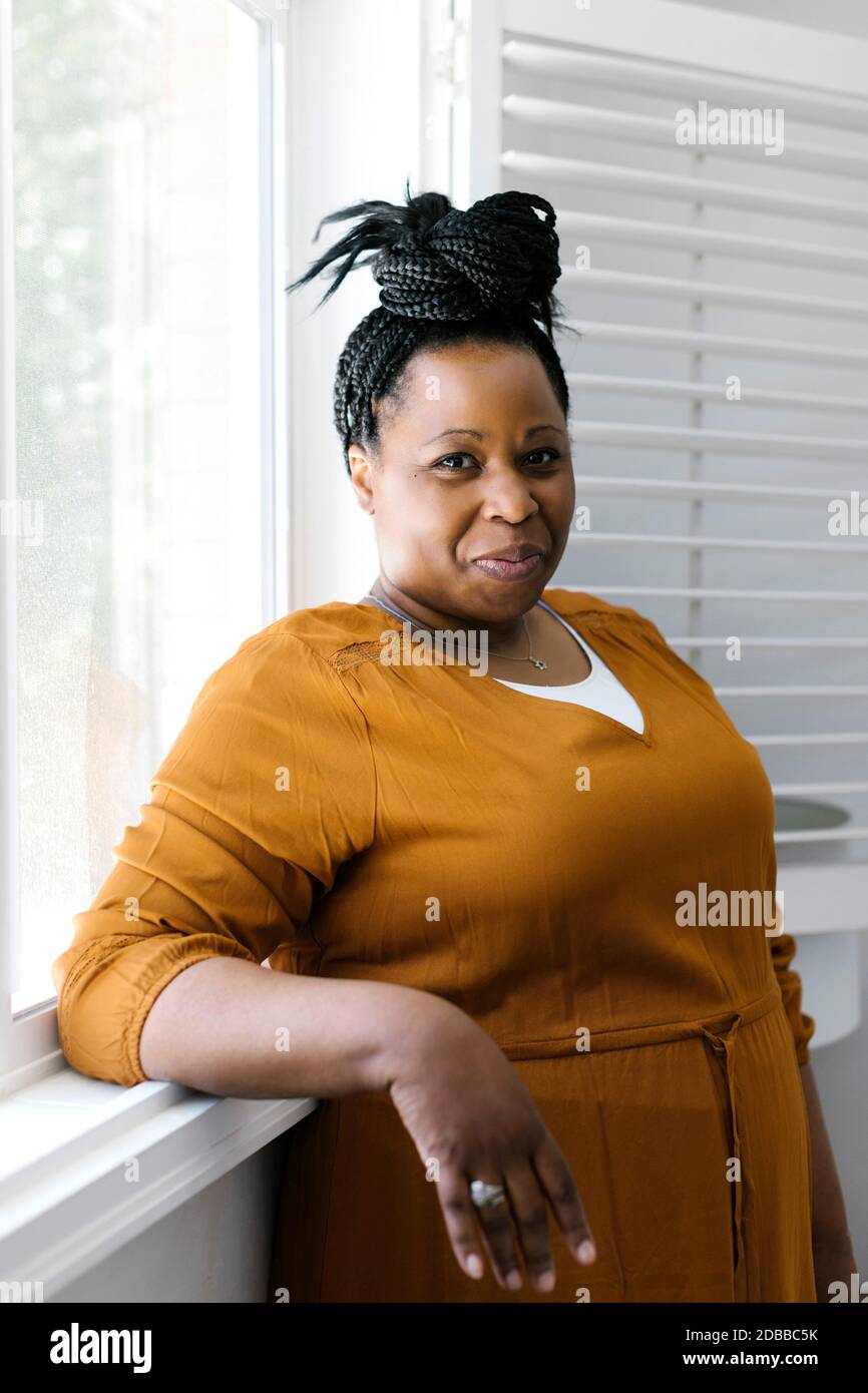 Portrait d'une femme souriante en robe orange debout près de la fenêtre Banque D'Images