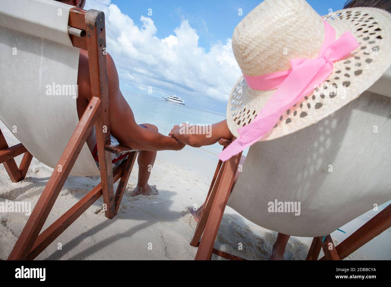 Vue arrière du couple sur la plage assis sur des chaises longues et tenir les mains Banque D'Images