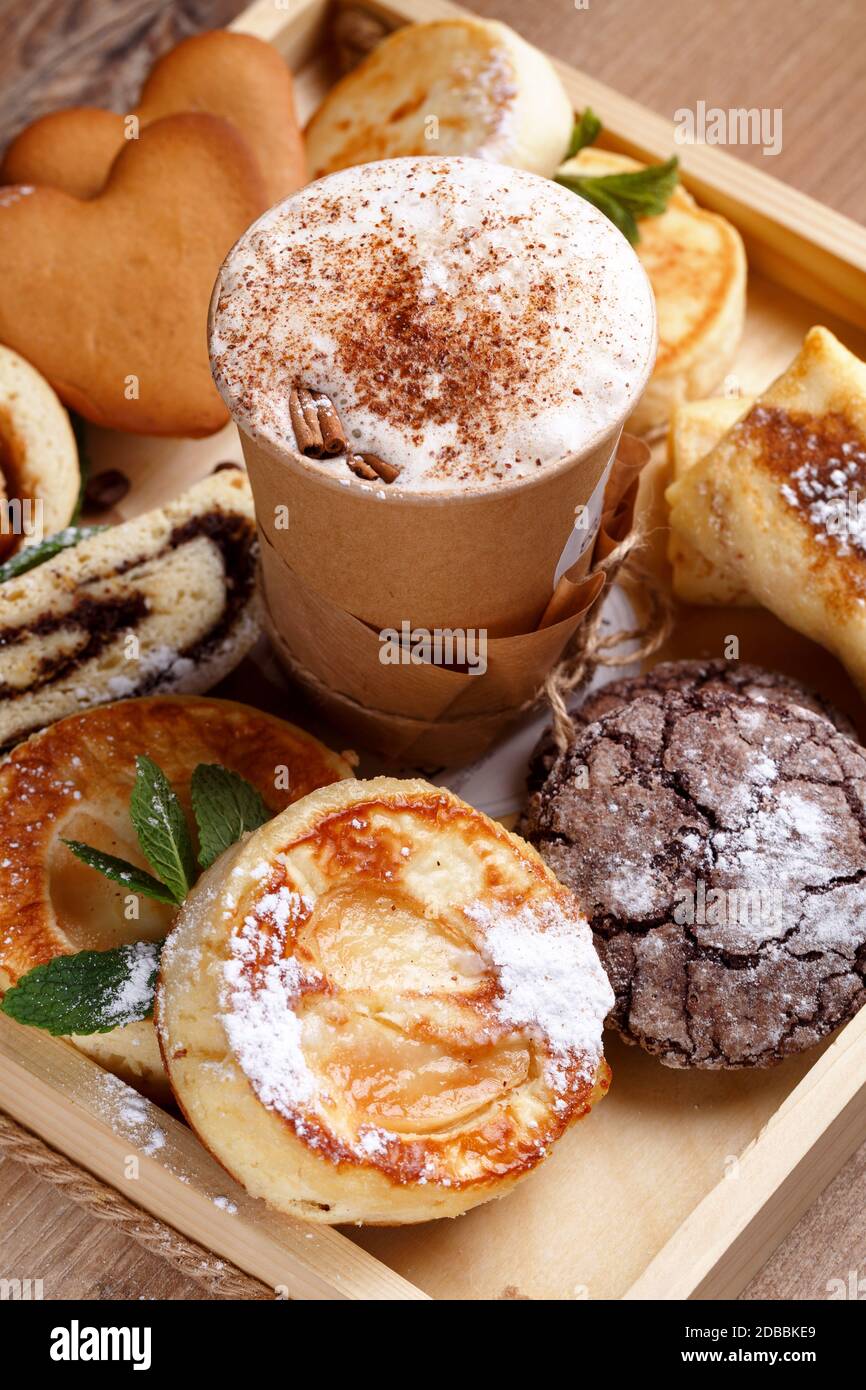 Café à la cannelle et biscuits au chocolat maison, strudel et fromages à la menthe. Desserts faits à la main et café dans une tasse en papier sur fond rustique brun en bois. Banque D'Images