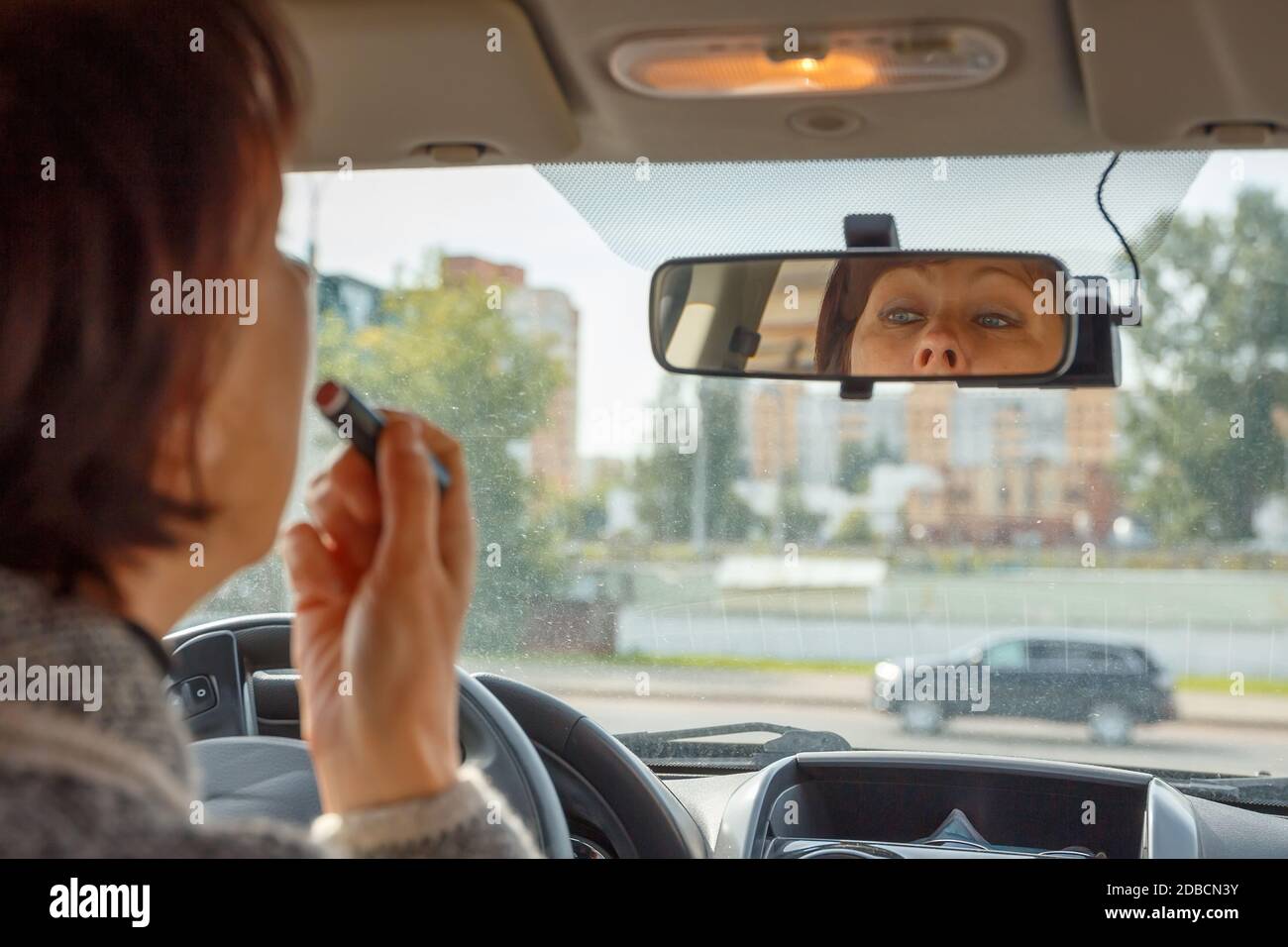 La femme regarde dans le rétroviseur intérieur de la voiture et peint ses  lèvres Photo Stock - Alamy