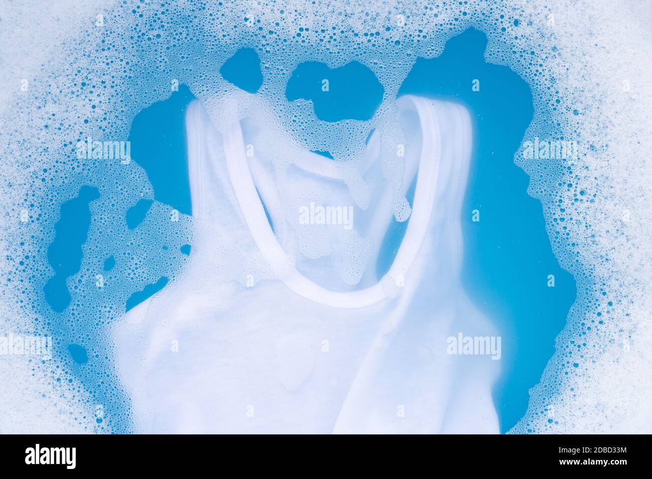 Maillot de chevreau blanc faire tremper dans de l'eau lessive bébé dissolution, lave-linge, fond bleu, concept de blanchisserie. Banque D'Images
