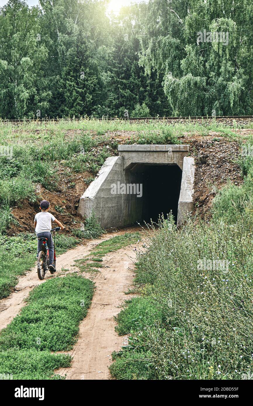 Un curieux garçon à vélo se déplace dans un tunnel sombre sous le chemin de fer dans la campagne Banque D'Images