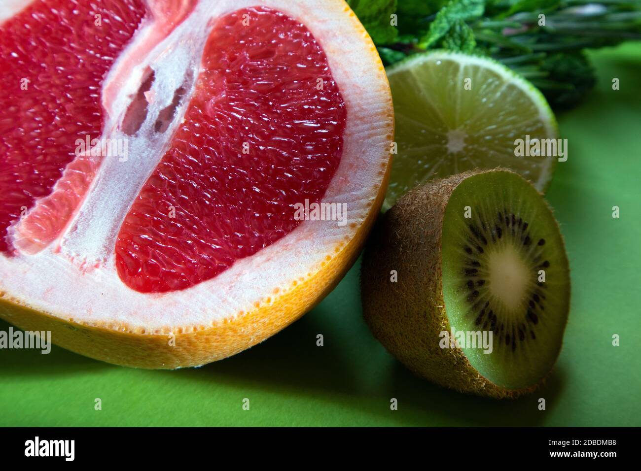 Composition fruitée d'orange rouge coupé, de citron vert, de kiwi et de verdure sur fond vert clair Banque D'Images