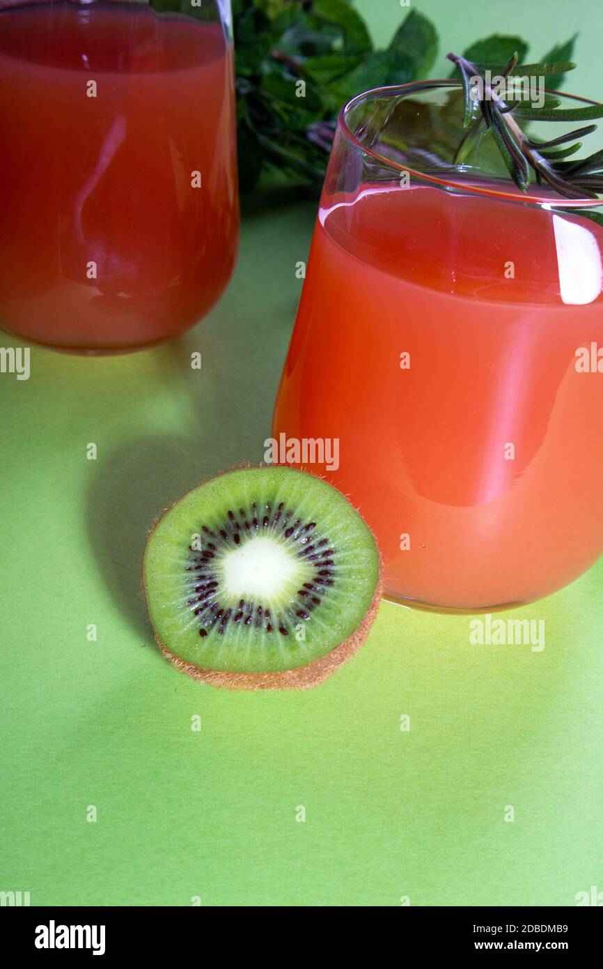 Composition de verres avec jus d'orange, citron vert, kiwi et verdure sur fond vert clair Banque D'Images