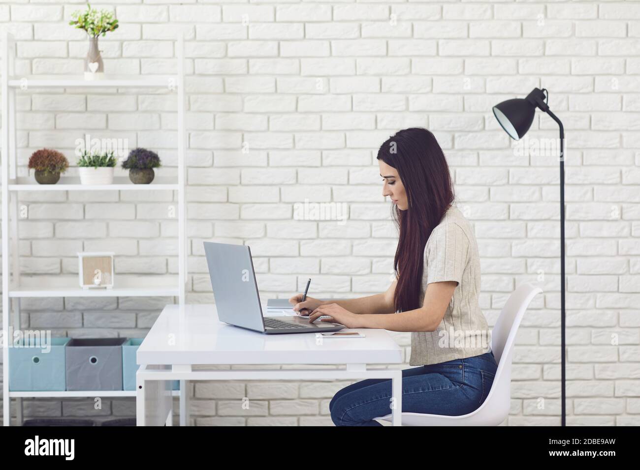 Femme assise avec un ordinateur portable et un ordinateur portable et prenant des notes pendant cours en ligne avec professeur Banque D'Images
