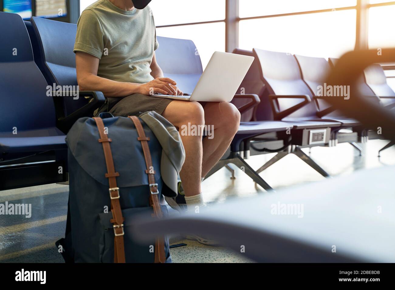 homme asiatique homme voyageur aérien avec masque noir assis dans la salle d'attente du terminal de l'aéroport en utilisant un ordinateur portable Banque D'Images